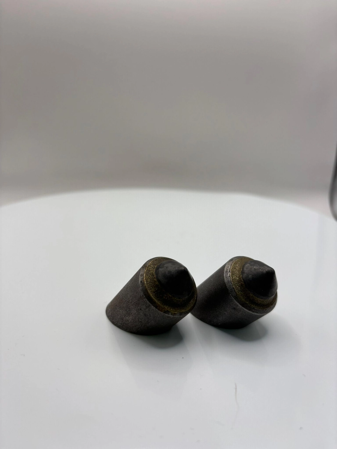 H-Tools - Hochleistungs-Gesteinsbohrkronen - Nahaufnahme von zwei gebrauchten oder abgenutzten kleinen, konischen Metallbohrern oder -einsätzen auf einem weißen, drehbaren Präsentationsständer.