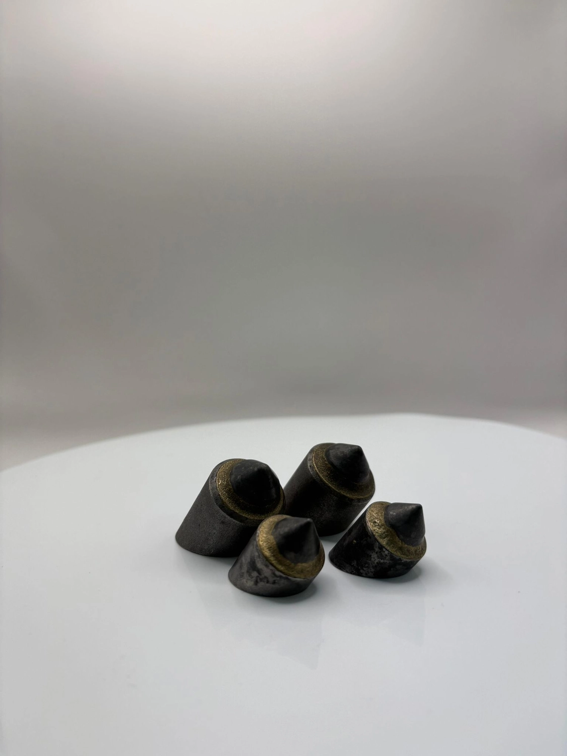 H-Tools - Hochleistungs-Gesteinsbohrkronen - Eine Gruppe von fünf schwarzen, leicht konischen oder gestuften Industrieschneidplatten auf einer weißen Oberfläche, aus einem niedrigen Winkel betrachtet.