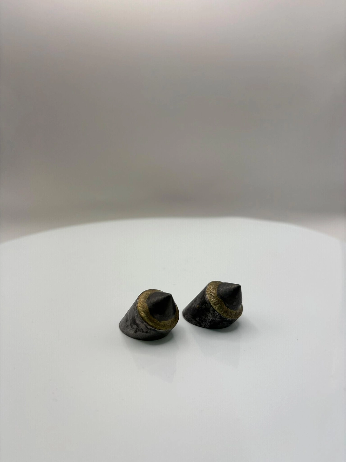 H-Tools - Hochleistungs-Gesteinsbohrkronen - Nahaufnahme von zwei gebrauchten oder abgenutzten kleinen, konischen Metallbohrern oder -einsätzen auf einem weißen, drehbaren Präsentationsständer.