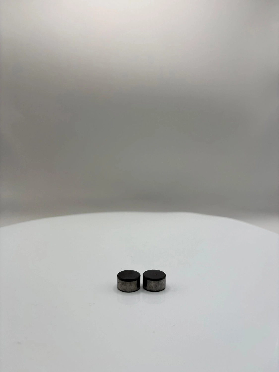 H-Tools - Hochleistungs-Gesteinsbohrkronen - Zwei schwarze, zylindrische Industrieschneidmaschinen stehen nebeneinander auf einer weißen, kreisförmigen Drehplattform vor einem neutralen Hintergrund.