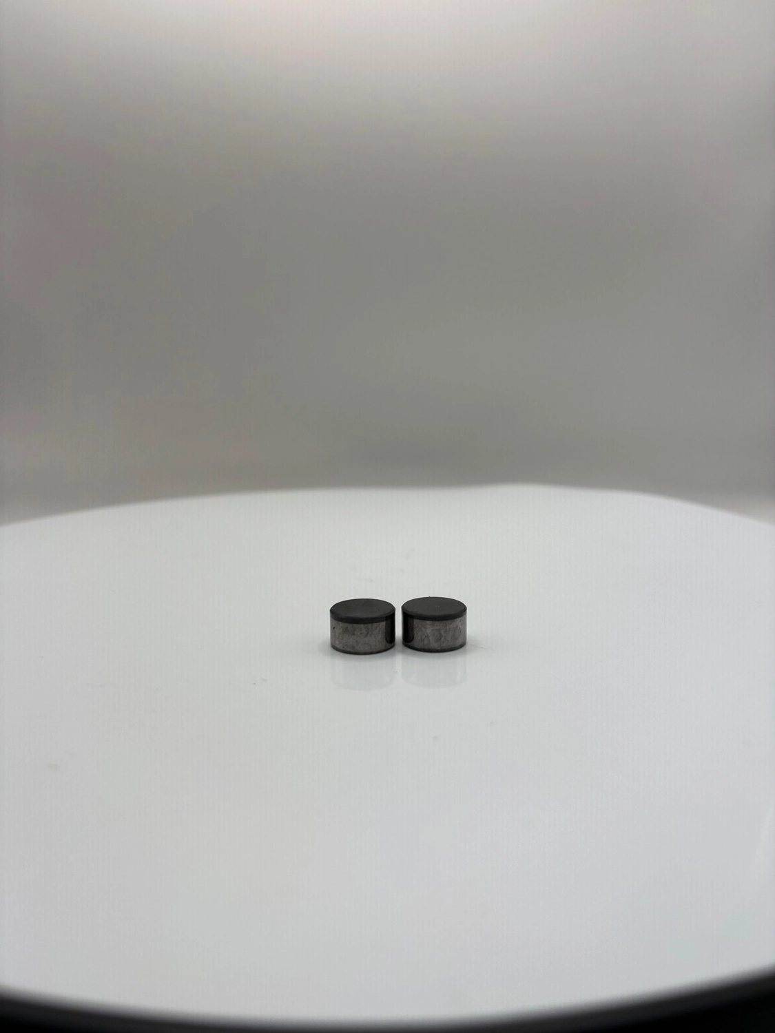 H-Tools - Hochleistungs-Gesteinsbohrkronen - Zwei schwarze, zylindrische Industrieschneidmaschinen stehen nebeneinander auf einer weißen, kreisförmigen Drehplattform vor einem neutralen Hintergrund.