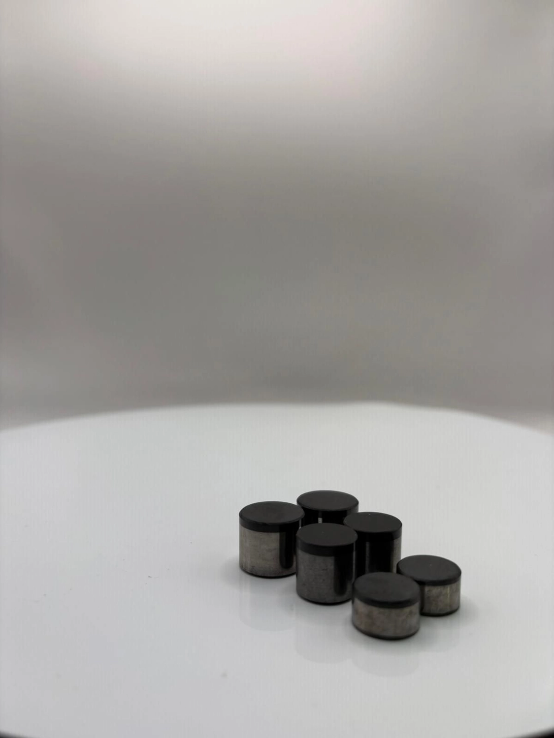 H-Tools - Hochleistungs-Gesteinsbohrkronen -Sechs schwarze, zylindrische Industrieschneidmaschinen, die auf einer weißen, kreisförmigen Drehplattform gruppiert sind, aus einem leichten Winkel betrachtet.