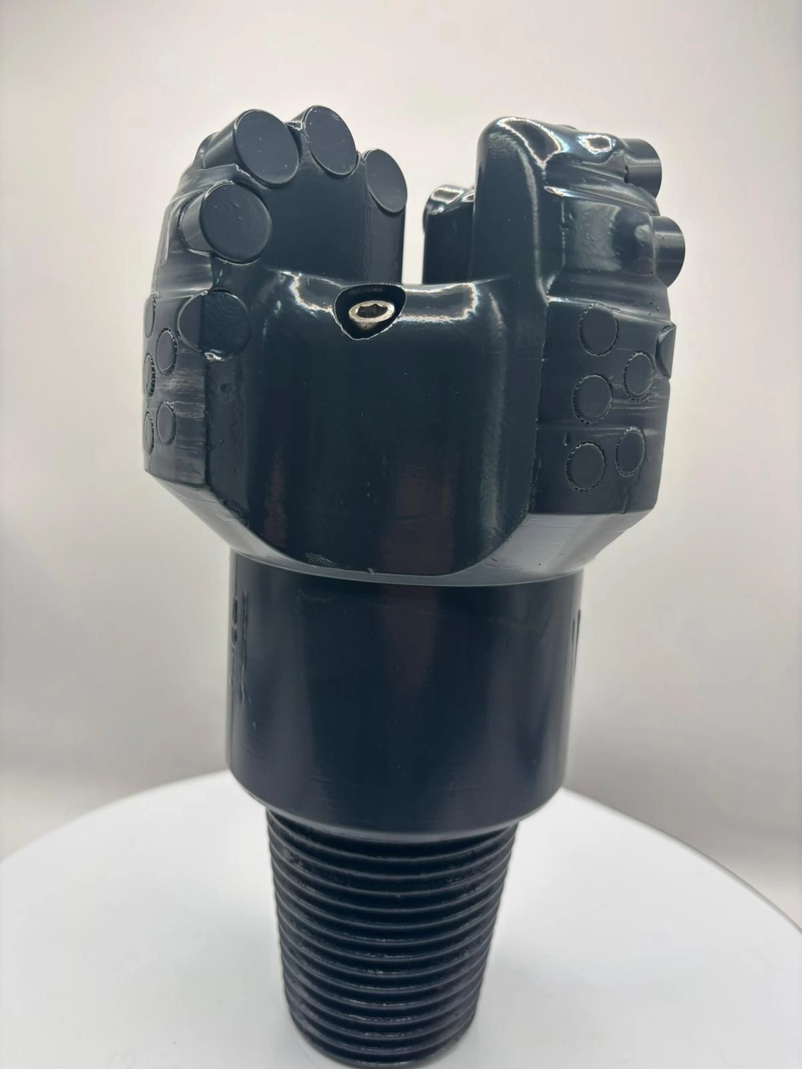 H-Tools - Hochleistungs-Gesteinsbohrkronen - Vorderansicht des großen, dunkelgrauen oder schwarzen Industriebohrkopfes, der an einem Schaft befestigt ist, auf einem weißen, drehbaren Ausstellungsständer.