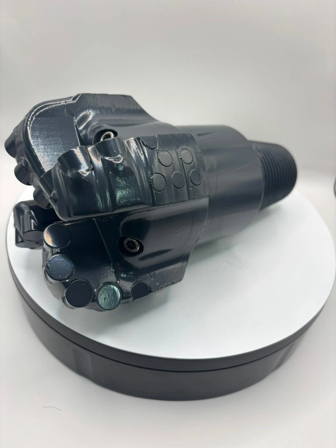 H-Tools - Hochleistungs-Gesteinsbohrkronen - Seitenansicht des großen, dunkelgrauen oder schwarzen Industriebohrkopfes, der an einem Schaft befestigt ist, auf einem weißen, drehbaren Ausstellungsständer.